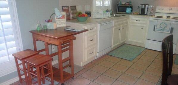 A kitchen with white cabinets, a wooden bar stool, a microwave, and a stove.