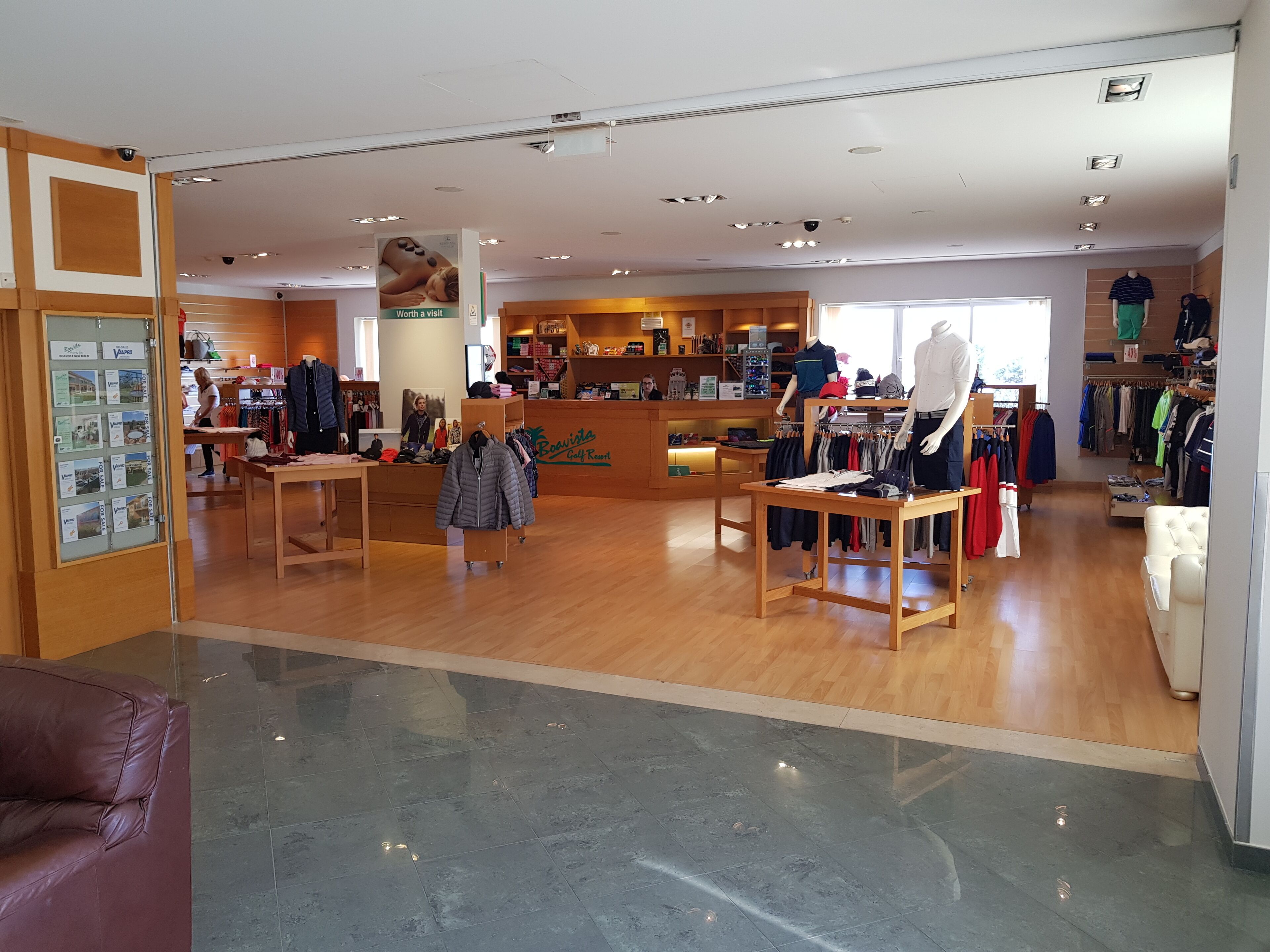 A clothing store with wooden flooring, clothing racks, and a counter.