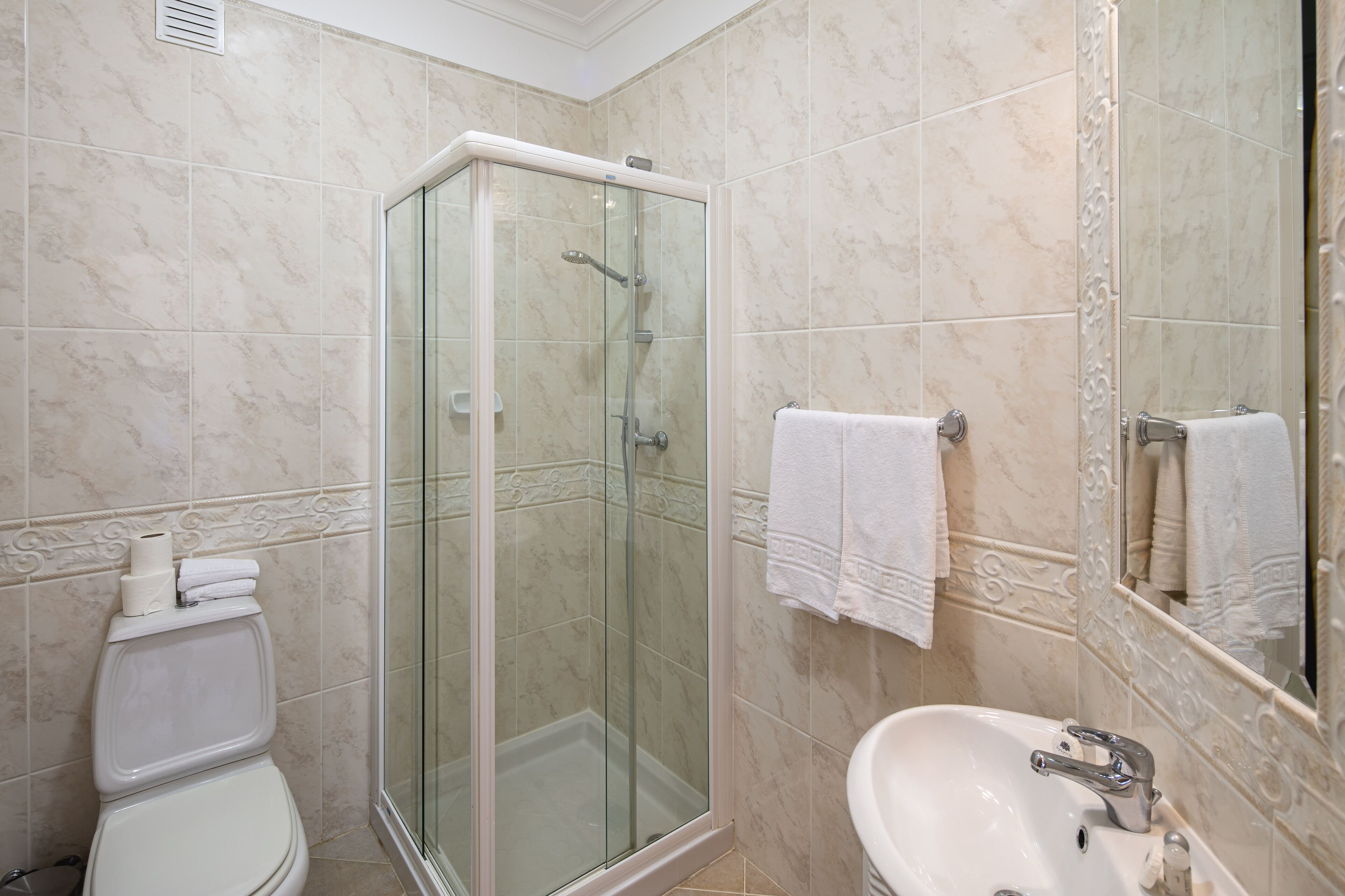 A bathroom with a glass-enclosed shower, a toilet, and a sink with a mirror.