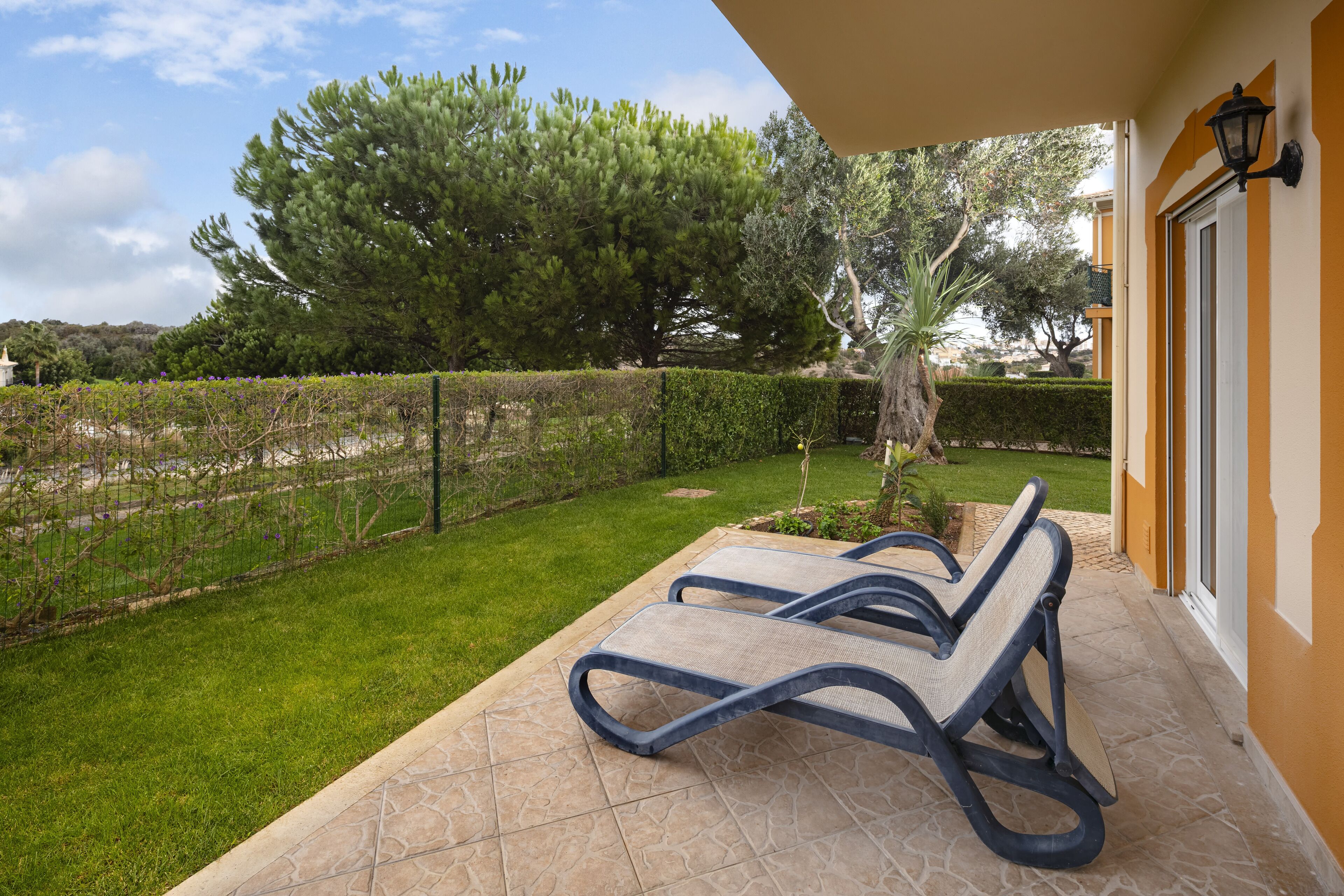 A patio with two lounge chairs, a well-maintained lawn, and a hedge.