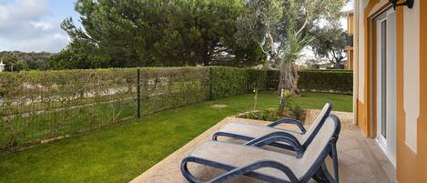 A patio with two lounge chairs, a well-maintained lawn, and a hedge.