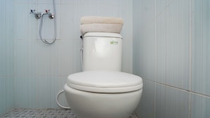 A toilet with a beige cover, a showerhead, and a wall-mounted faucet. - OYO 1765 Herman Homestay (Wonokitri)