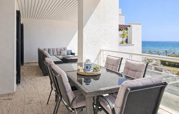 Uma varanda com mesa, cadeiras e vista para o mar.