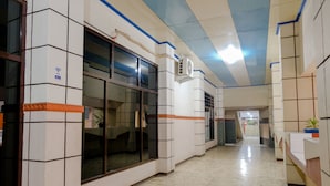 Un couloir d’hôtel aux murs recouverts de carreaux, avec une grande fenêtre et un plafond doté d’un éclairage fluorescent.