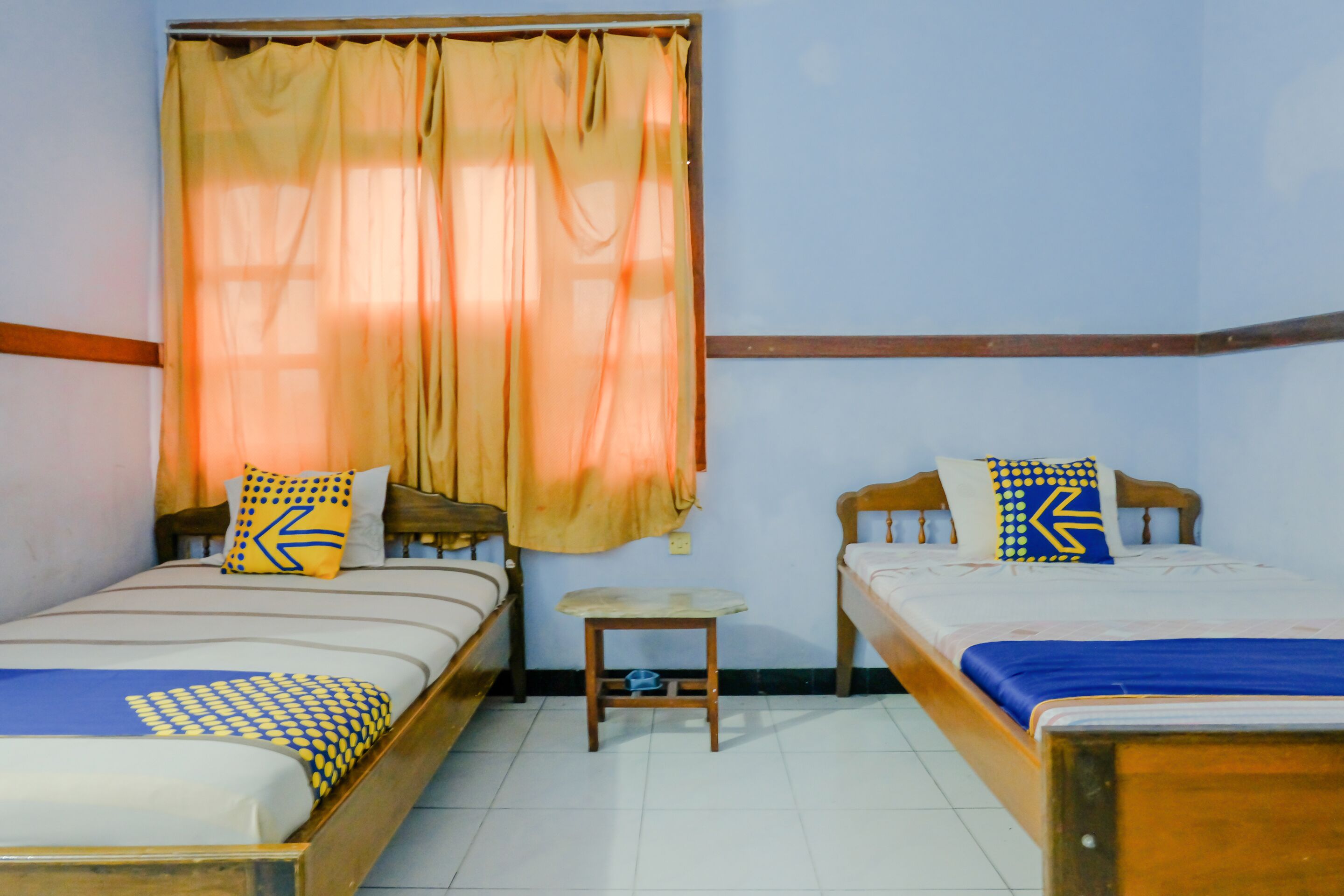 A room with two single beds, a small table, and a window with curtains.