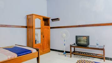 A room with a bed, a wooden wardrobe, a television on a small table, and a standing fan.