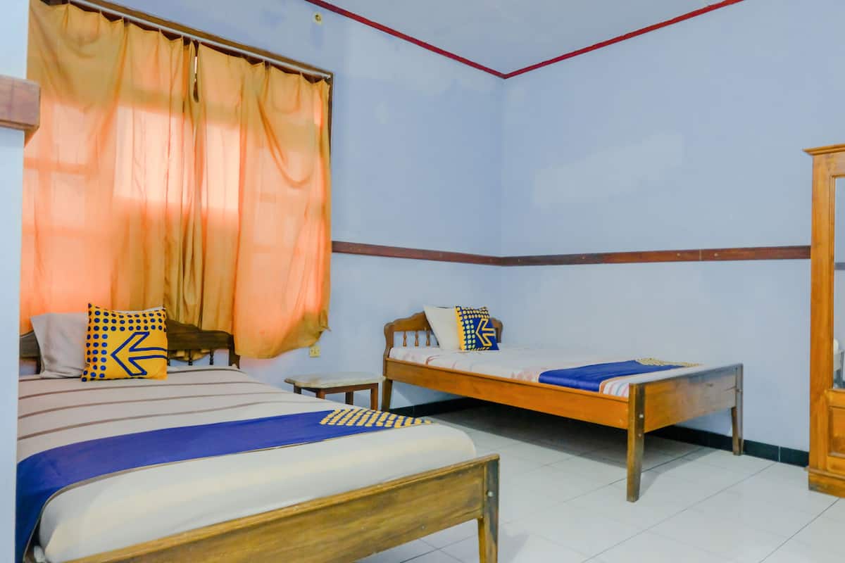 Una habitación con dos camas de madera, una con cubrecama azul y otra con cubrecama blanca. Hay una mesita de noche de madera con una lámpara junto a las camas.