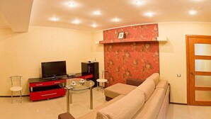 Una sala de estar con un sofá, un televisor sobre un mueble bajo, una mesita y un aparador rojo.