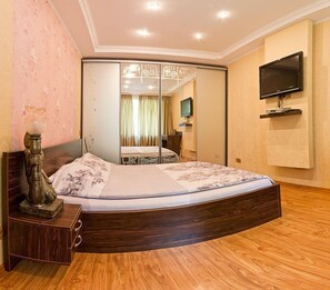 A bedroom with a large bed, a TV mounted on the wall, and a mirror cabinet.