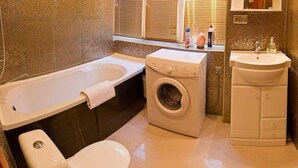 Un baño pequeño con bañera, lavadora, inodoro y lavamanos.