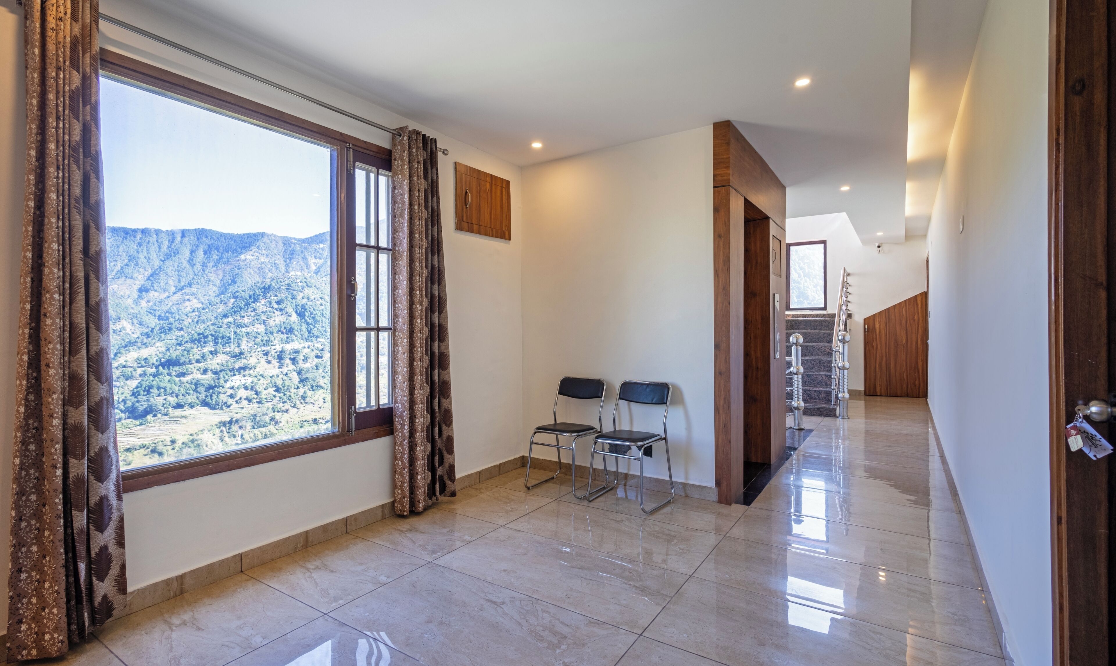 Habitación amplia con un gran ventanal que ofrece vistas a la montaña, una escalera que conduce a otro nivel y dos sillas cerca de la ventana.