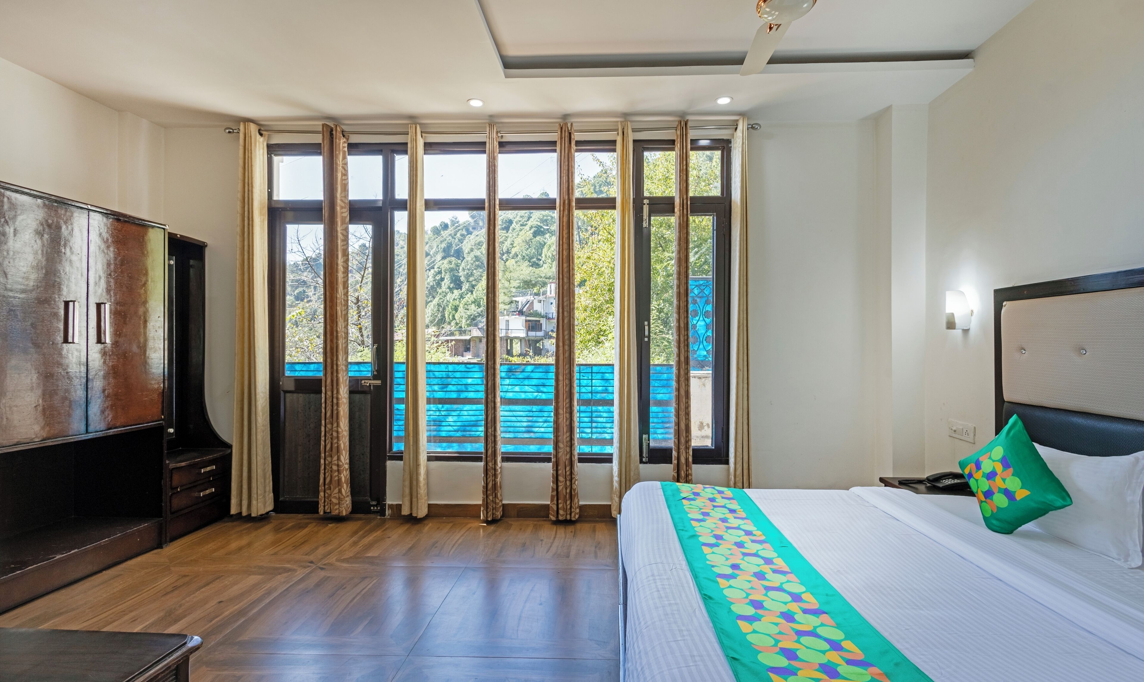 A hotel room with a bed, a TV, and a view of a blue railing outside.