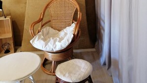 A wicker chair with a cushion, a small round table, a mirror on the wall, and a curtain. - Chambres d'Hotes la Source (Mareuil-Sur-Lay-Dissais)