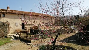 A rustic stone house with a tiled roof, a garden with blooming trees, and a stone wall. - Chambres d'Hotes la Source (Mareuil-Sur-Lay-Dissais)