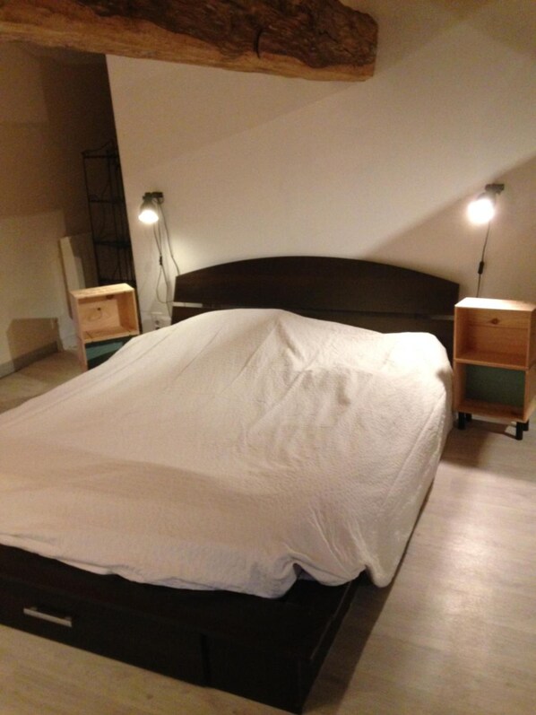 A bedroom with a large bed, wooden headboard, bedside tables, and wall-mounted lamps.
