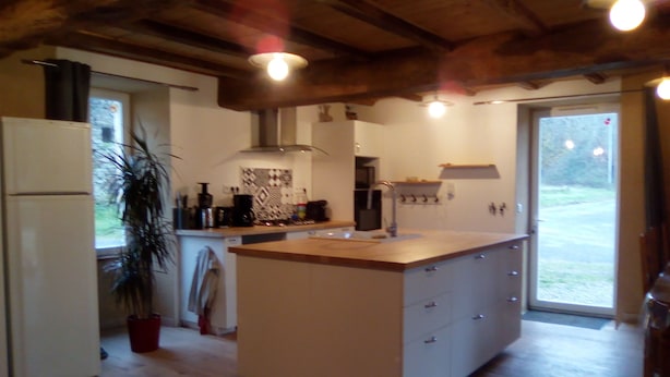 A kitchen with a central island, wooden ceiling beams, and a large window. - Chambres d'Hotes la Source (Mareuil-Sur-Lay-Dissais)