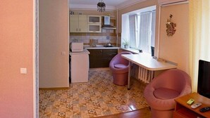 A compact kitchen with a microwave, a sink, and a window with blinds. There are two pink chairs and a small table. The floor has a patterned tile design. - Apart Kiev Starokievskiy pereulok 5-1 (Kyiv)