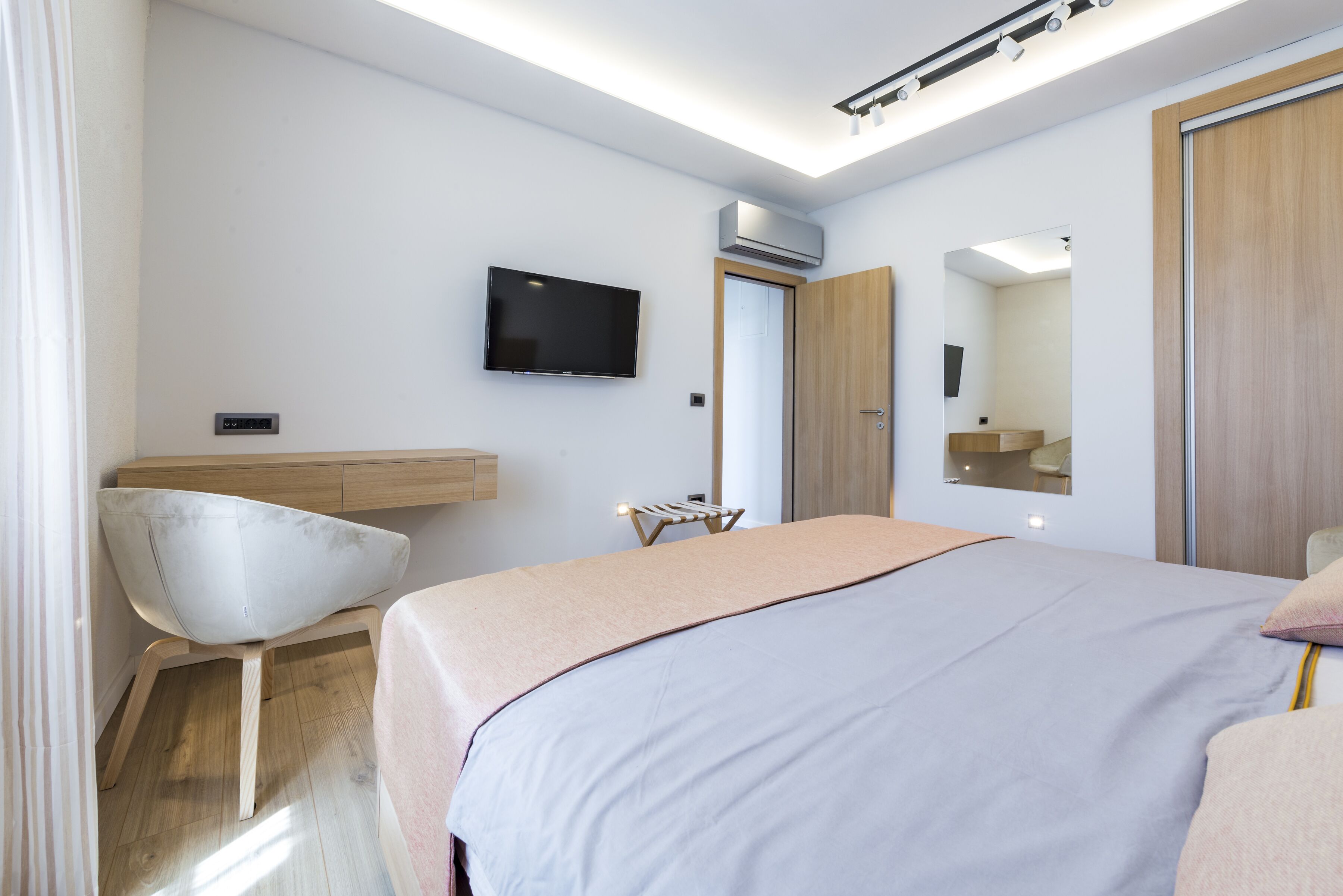 Ein modernes Hotelzimmer mit Bett, Schreibtisch, Stuhl, Fernseher und Klimaanlage.