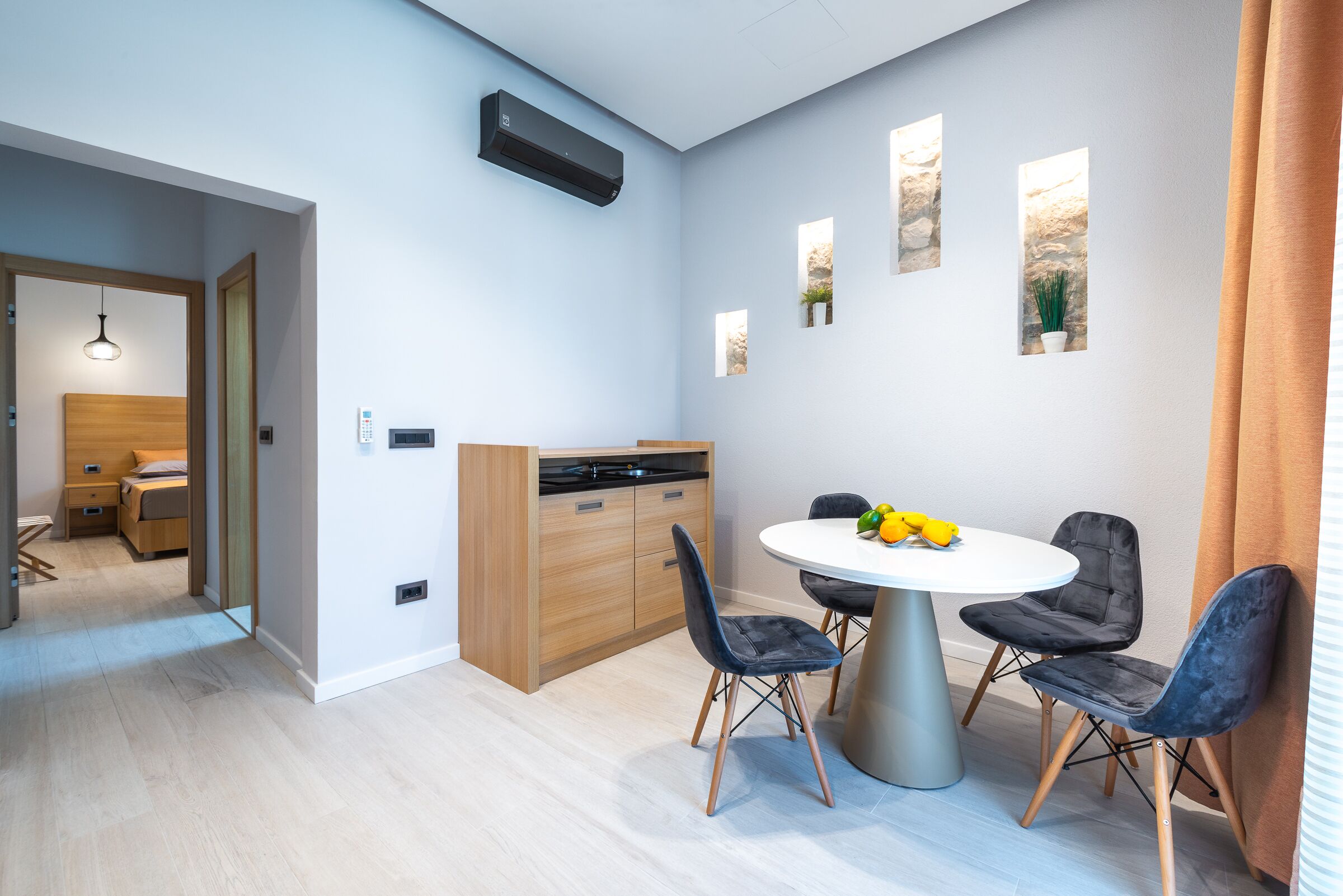 Una cocina moderna con estufa integrada, una zona de comedor con una mesa redonda y dos sillas, y una ventana pequeña con una planta.