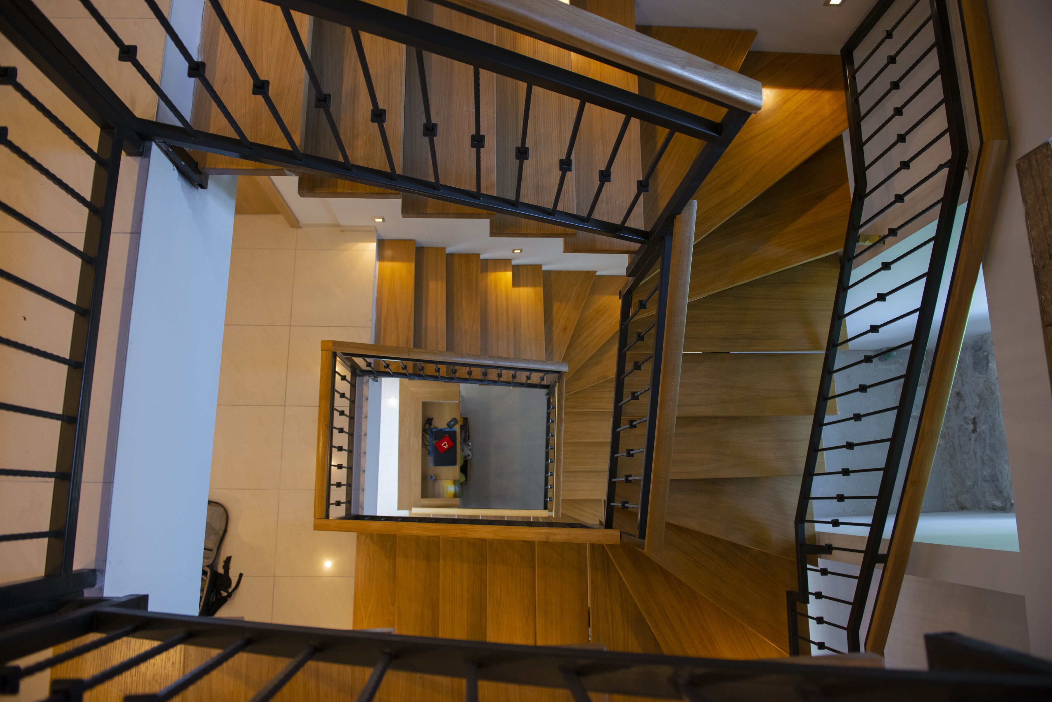 Una escalera moderna con escalones de madera y barandillas metálicas, que conduce a un rellano con vistas del interior.
