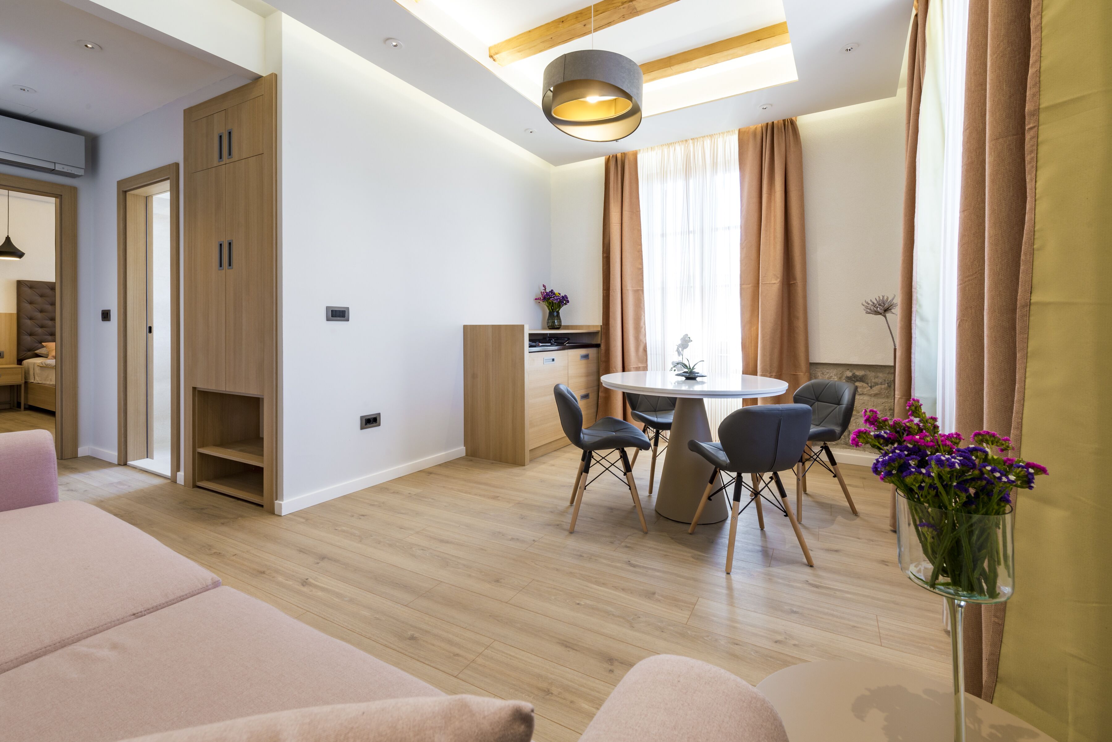 A modern living room with a dining area, wooden flooring, and a large window with curtains.