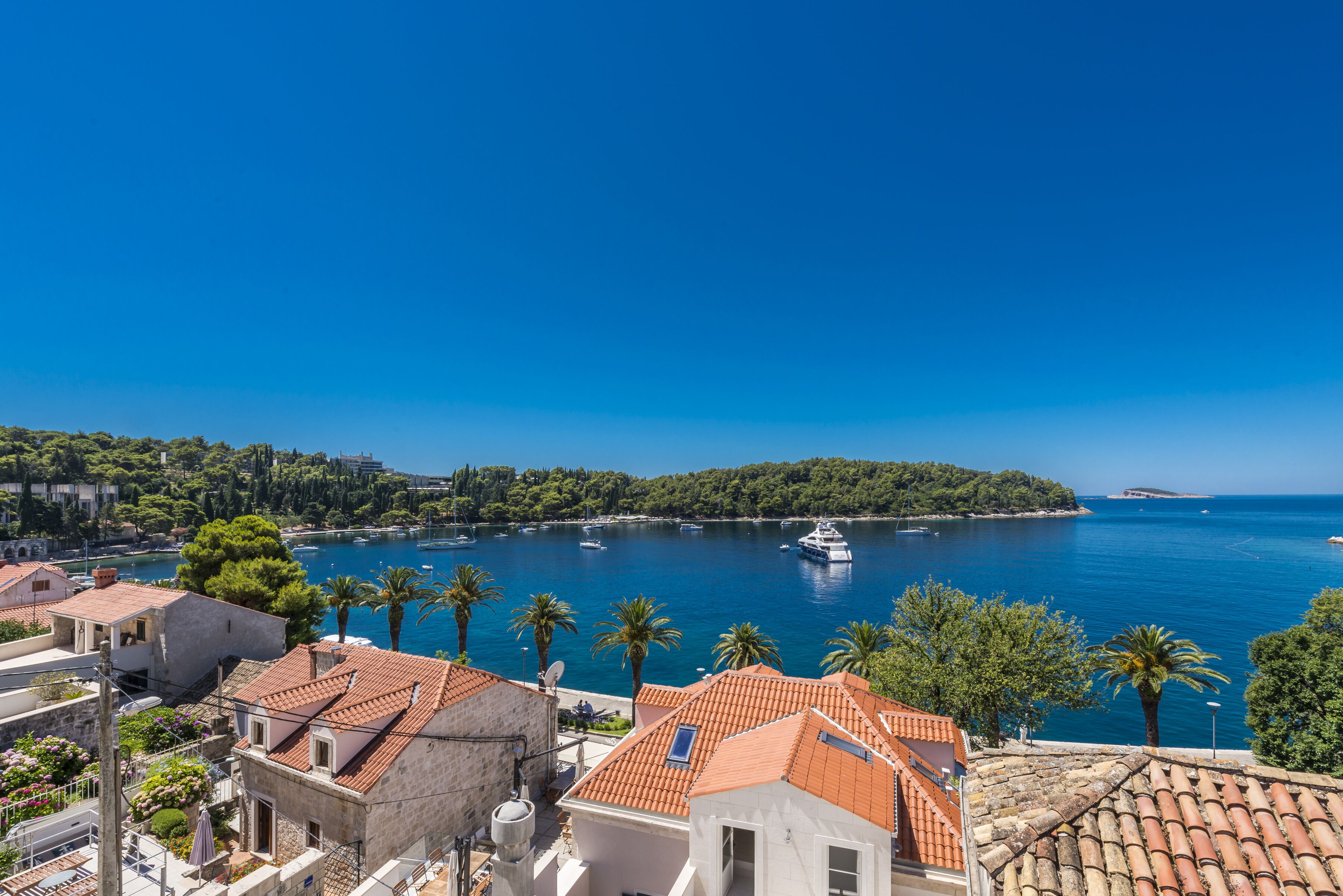 Un pueblo costero con edificios de tejados terracota, un puerto deportivo con barcos y un cielo azul despejado.