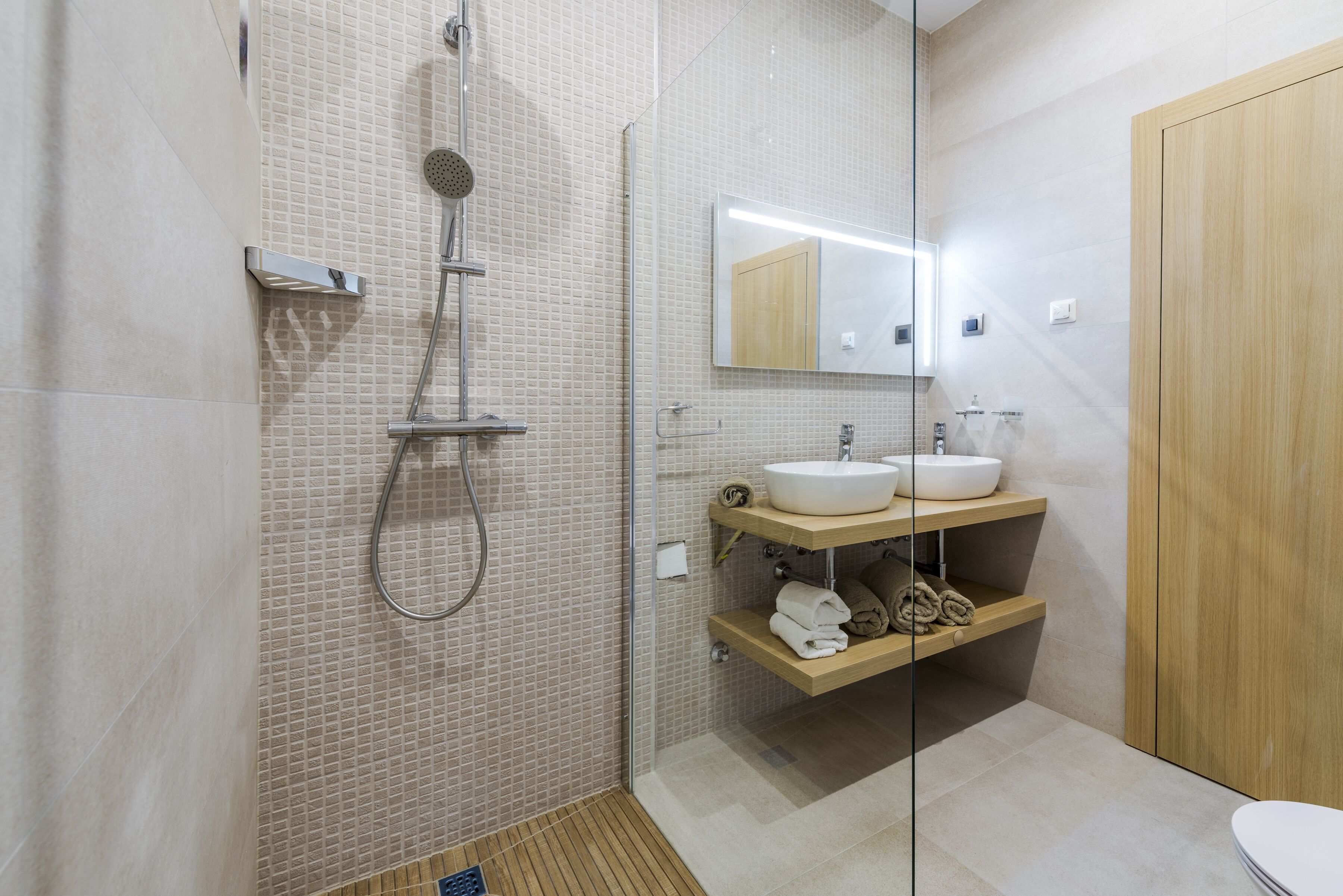 A modern bathroom with a glass shower enclosure, two sinks, and a wooden vanity.