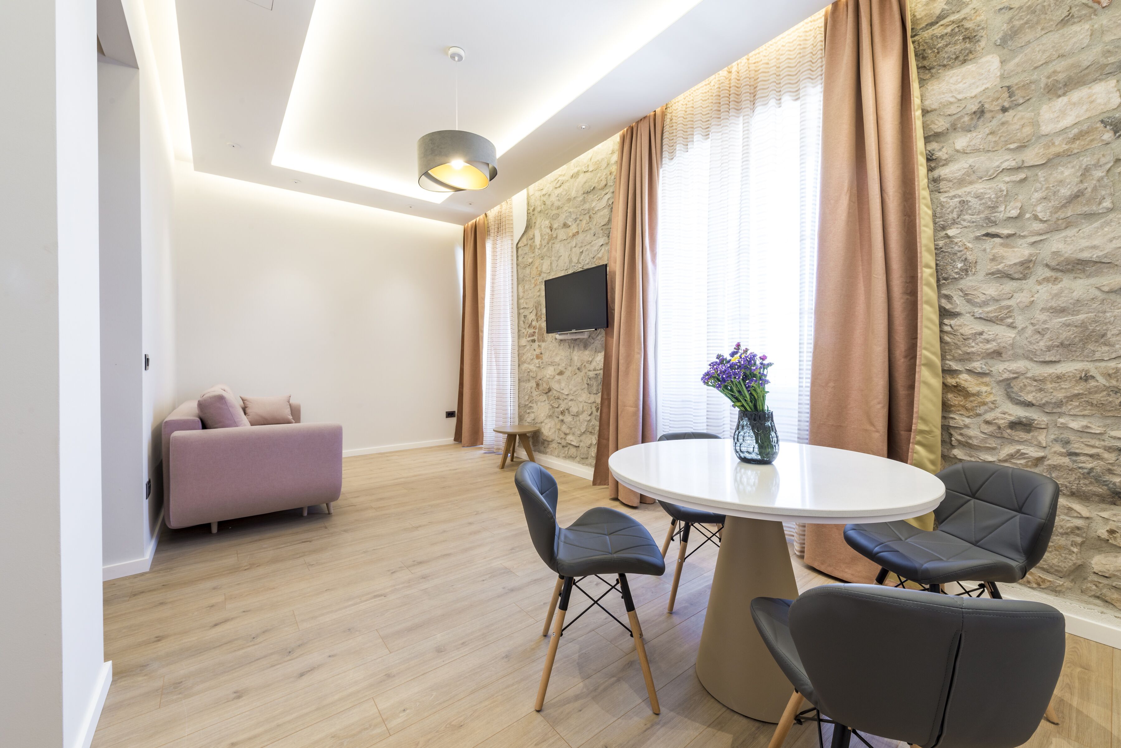 A modern living room with a sofa, a dining table with chairs, and a stone wall.