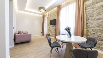 A modern living room with a sofa, a dining table with chairs, and a stone wall.