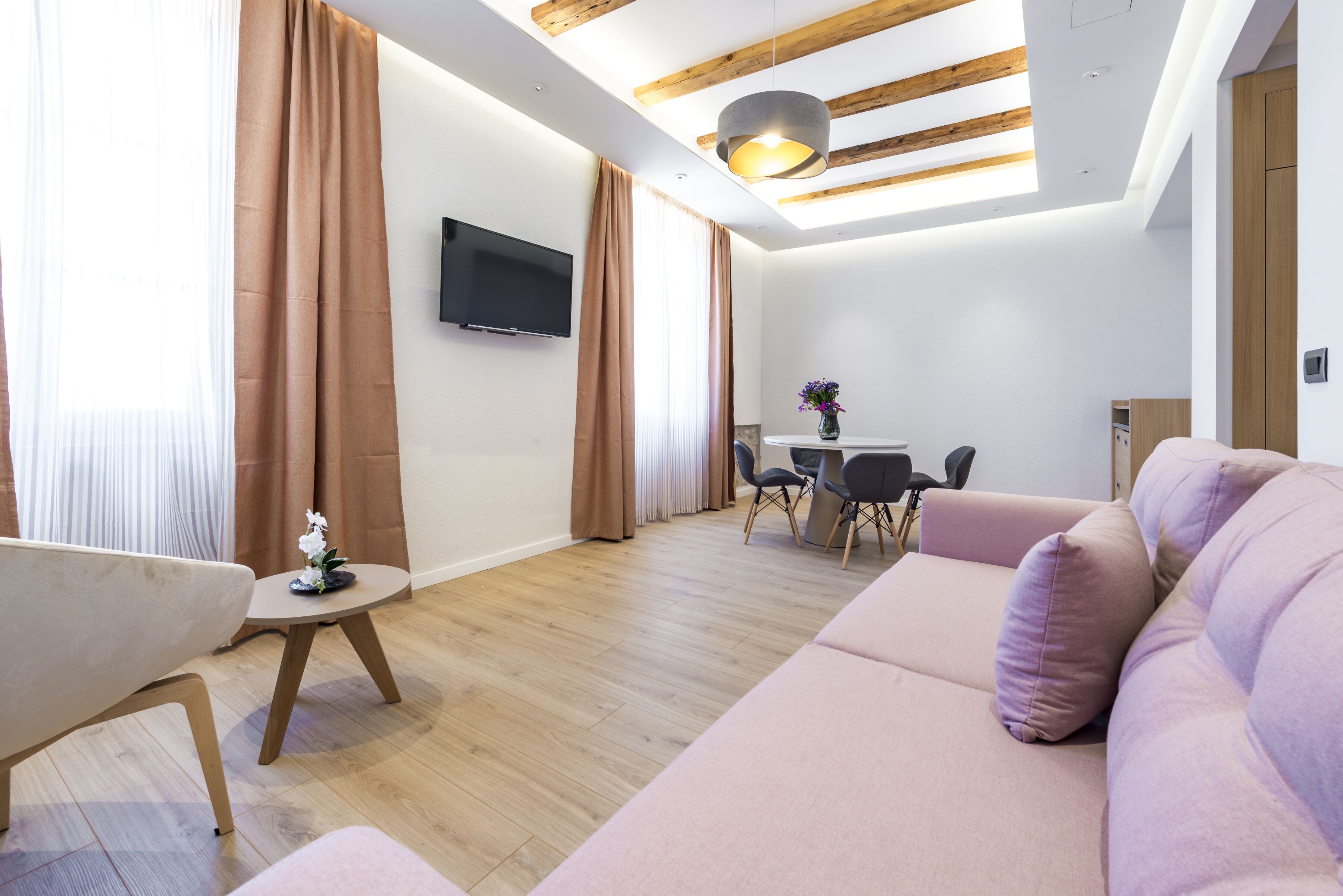 A modern living room with a sofa, a small table, and a TV mounted on the wall.