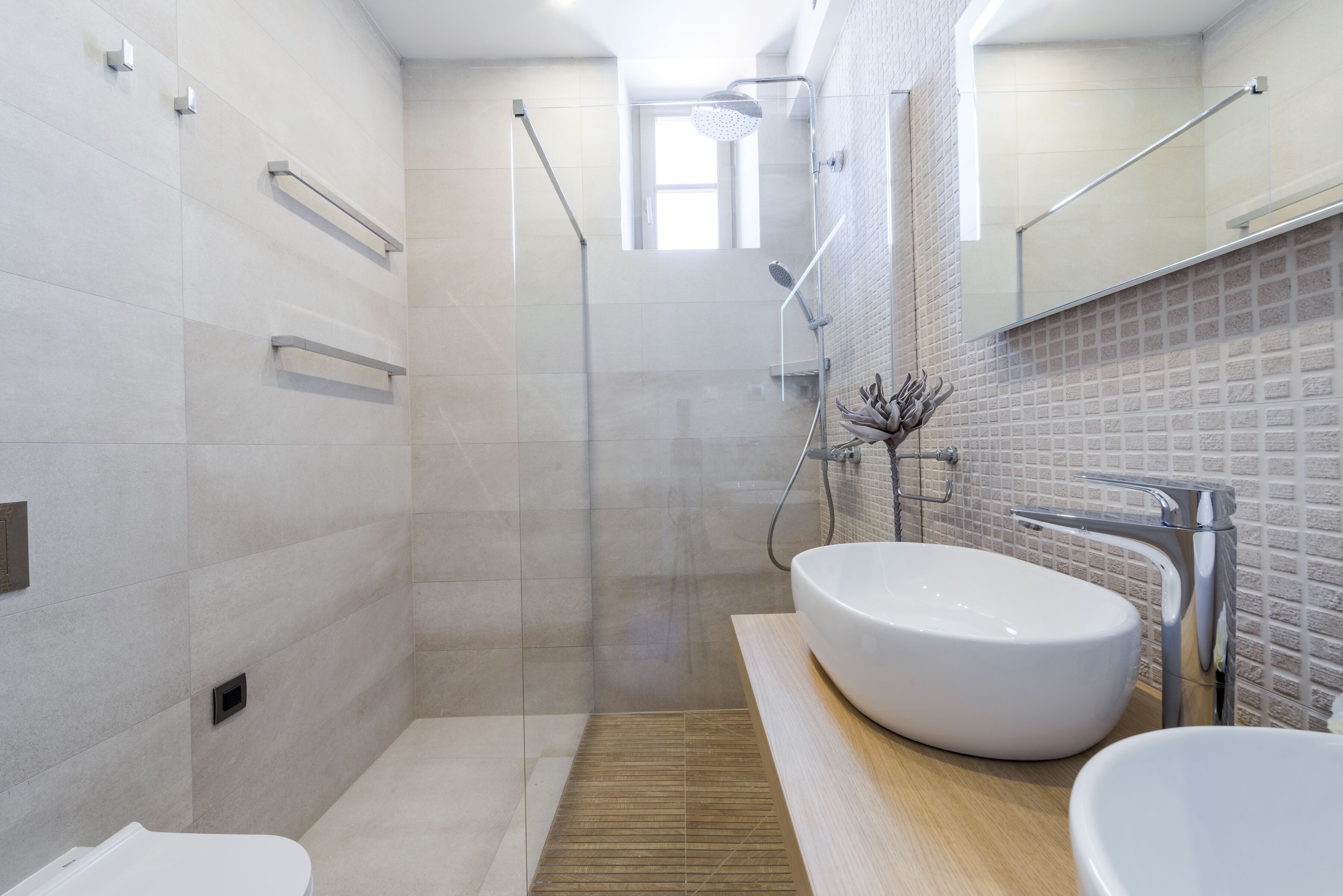 A modern bathroom with a large shower, a white sink, and a wooden vanity.