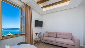 Una sala de estar moderna con un ventanal grande, un sofá rosa, un televisor de pantalla plana y una mesita auxiliar con un jarrón de flores.