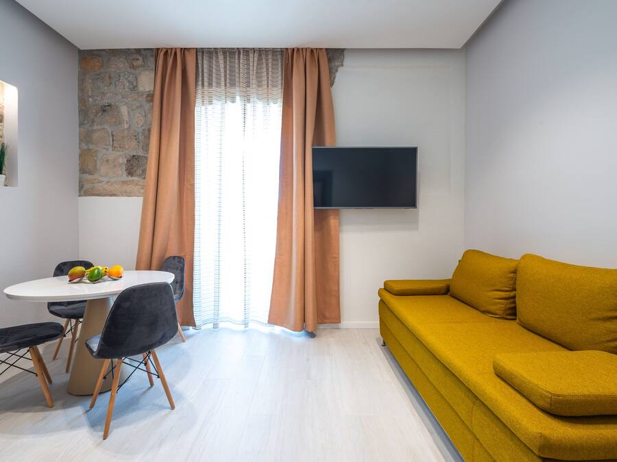 Un salon moderne comprenant un canapé, une table à manger avec des chaises, un téléviseur à écran plat fixé au mur et un mur d’accent en pierre.
