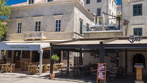 Un bistró y bar de vinos con terraza, un cartel y un edificio con techo de tejas.