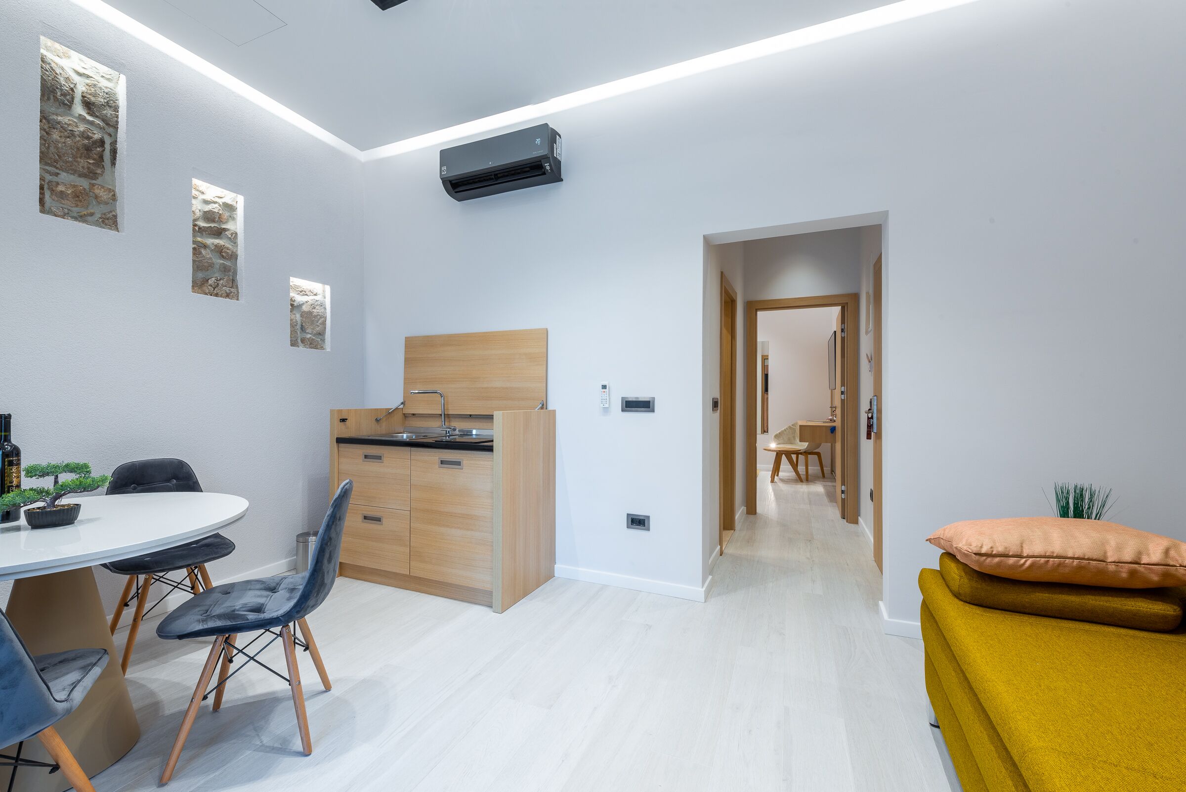 Una cocina moderna con encimera de madera y horno empotrado, una zona de comedor con una mesa redonda y sillas, y una acogedora sala de estar con un sofá amarillo.