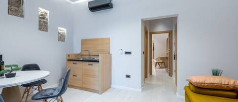 Una cocina moderna con encimera de madera y horno empotrado, una zona de comedor con una mesa redonda y sillas, y una acogedora sala de estar con un sofá amarillo.