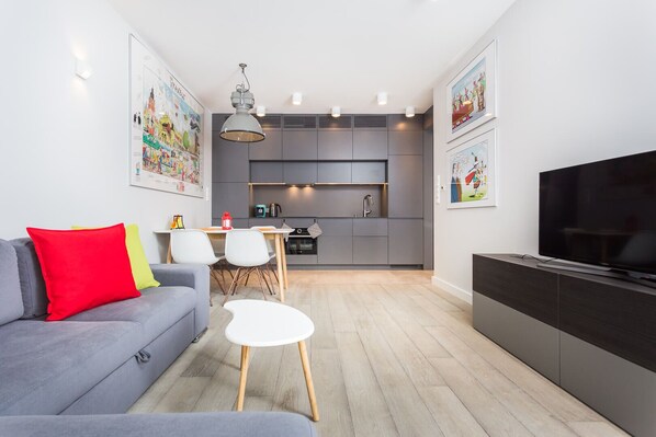 A modern living room with a grey sofa, a small white table, and a TV on a dark cabinet.