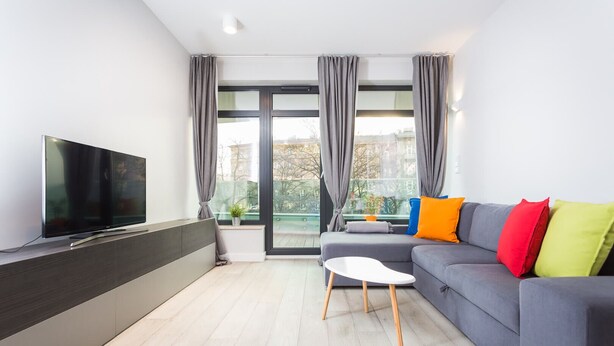 A modern living room with a flat-screen TV, grey sofa, colorful cushions, and a small white table. - 2- bedroom Apartment near Main Market Square (kraków)