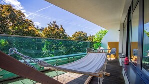 A balcony with a hammock, a table, and chairs, overlooking a green area with trees. - 2- bedroom Apartment near Main Market Square (kraków)