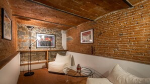Una habitación acogedora con pared de ladrillo, una mesa redonda de cristal, un sofá blanco y dos cuadros enmarcados.