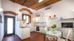 Una cocina compacta con horno integrado, una mesa de comedor con sillas y un televisor en la pared.
