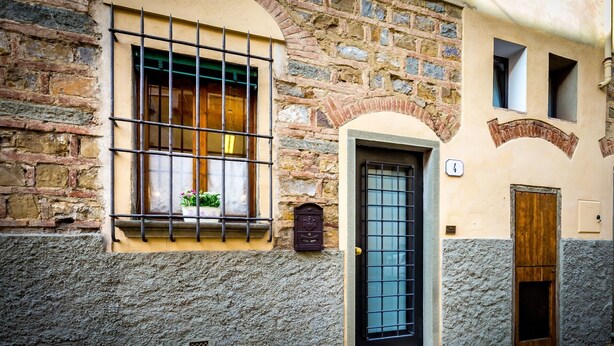 Un edificio de piedra con una ventana de barrotes metálicos, una puerta de madera y una pequeña ventana con una planta.