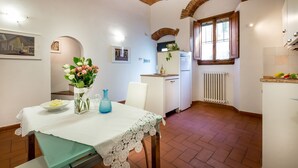 Un comedor con una mesa preparada para dos, una cocina con refrigerador y ventana, y un piso de baldosas.
