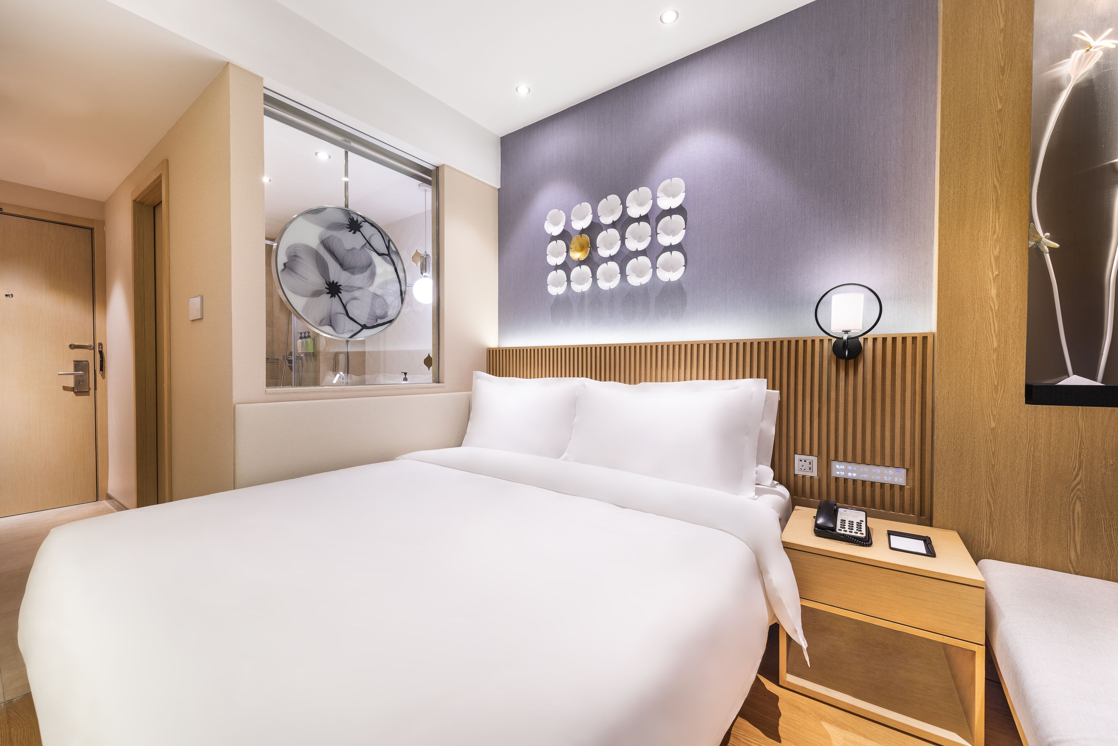 Una moderna camera d'albergo con un letto grande, un comodino con il telefono, una lampada a parete e un pannello decorativo.