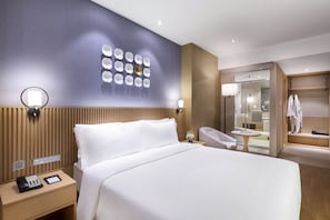 A modern hotel room with a large bed, bedside table with a phone and tablet, a wall-mounted light, and a bathroom visible through an open door. - Crystal Orange Hotel  Wangfujing Street (Beijing)