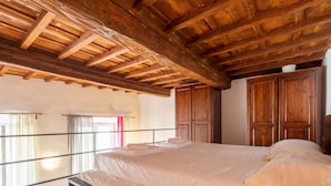 A bedroom with a large bed, wooden ceiling beams, and a view of the outdoors.