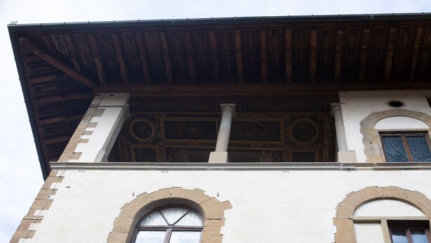 A building with a white facade, two arched windows, and a wooden roof structure.