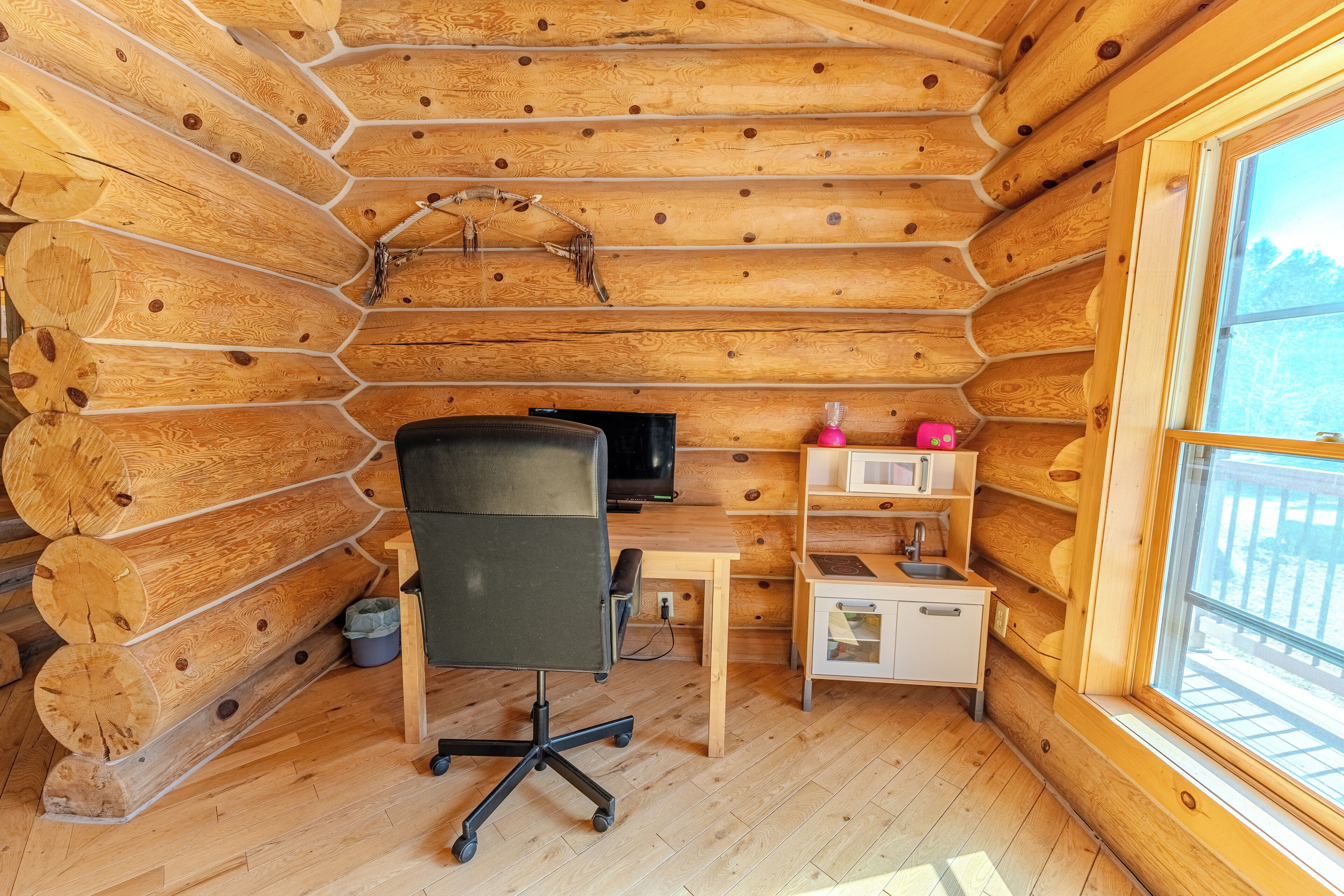 Interior de una cabaña de troncos con un escritorio de madera, una silla de oficina y una ventana.
