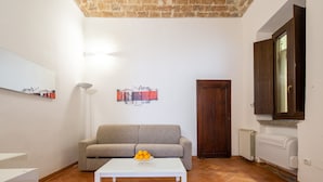 Een woonkamer met een bank, een bijzettafeltje met fruit, een radiator en een deur.