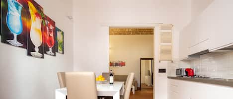 Une cuisine moderne avec des meubles blancs, une bouilloire rouge et un coin repas comprenant une table et des chaises blanches.